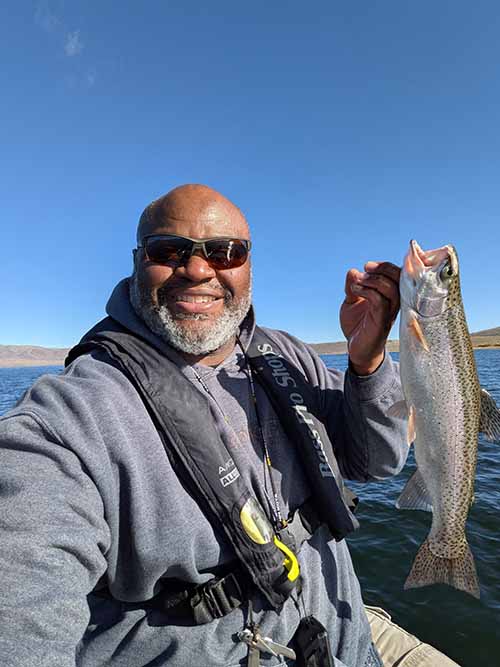 James Hadley sits by a lake showing off a fish.